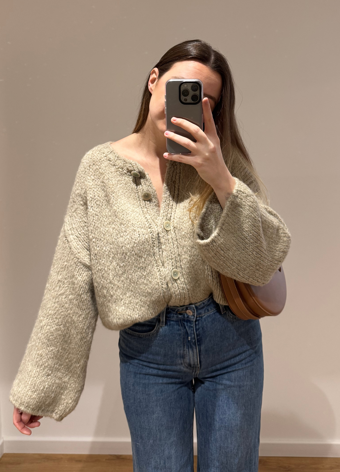 Zoom sur une femme portant un gilet droit beige LOU en coton à boutons argenté, avec un jean droit à ourlets ALEXIA, vue en intérieur sur parquet et fond blanc.