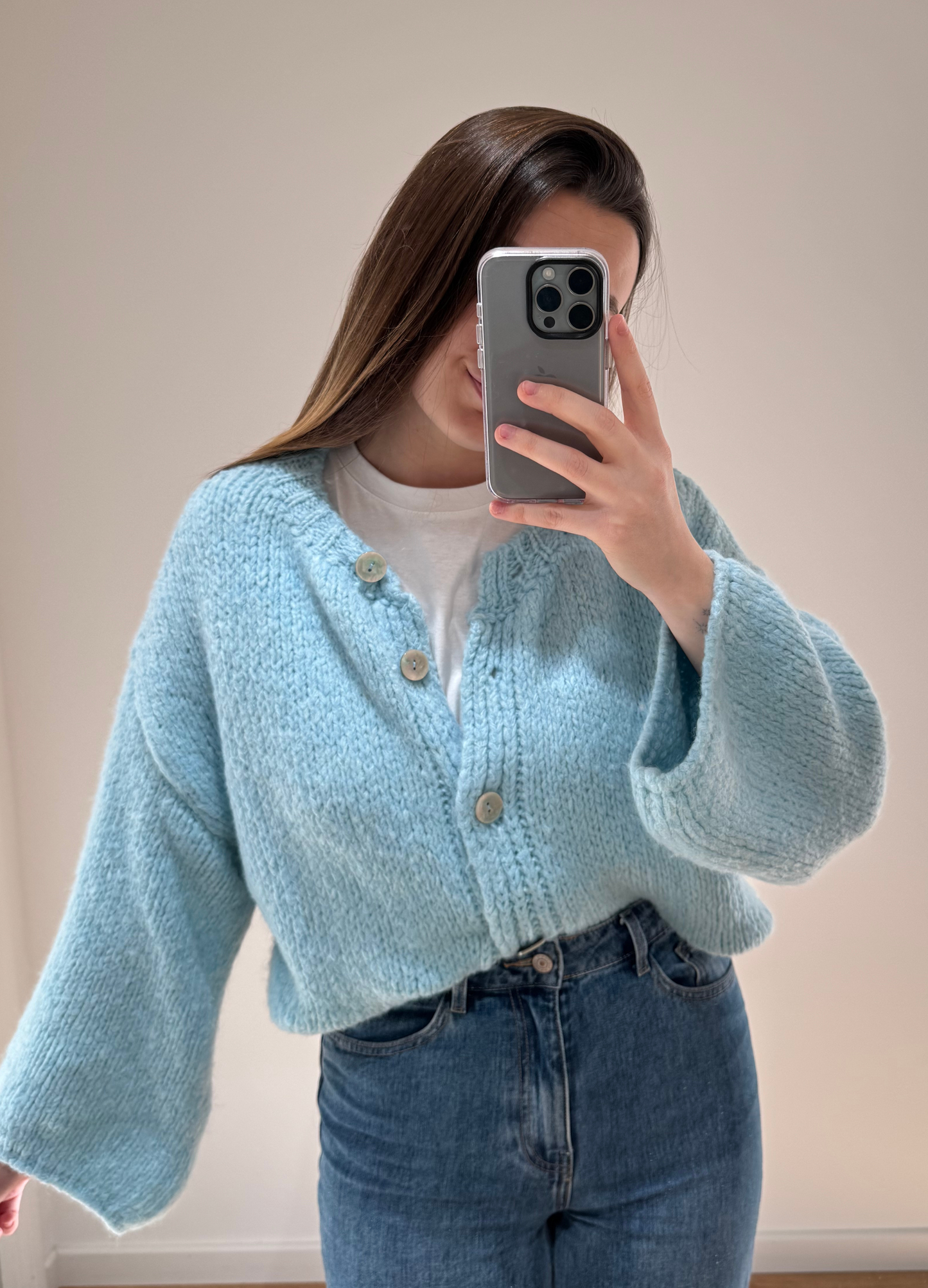 Zoom sur une femme portant un gilet droit bleu LOU en coton à boutons argenté, avec un jean droit à ourlets ALEXIA, vue en intérieur sur parquet et fond blanc.