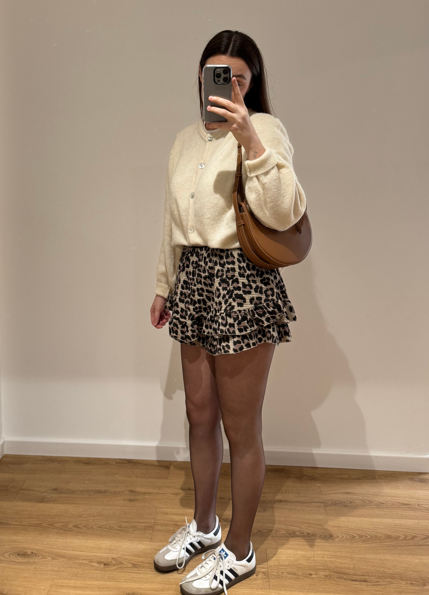 Femme portant un cardigan blanc OLIVIA en coton à boutons argenté, avec un short à motifs léopard KLEOFINA , vue en intérieur sur parquet et fond blanc.