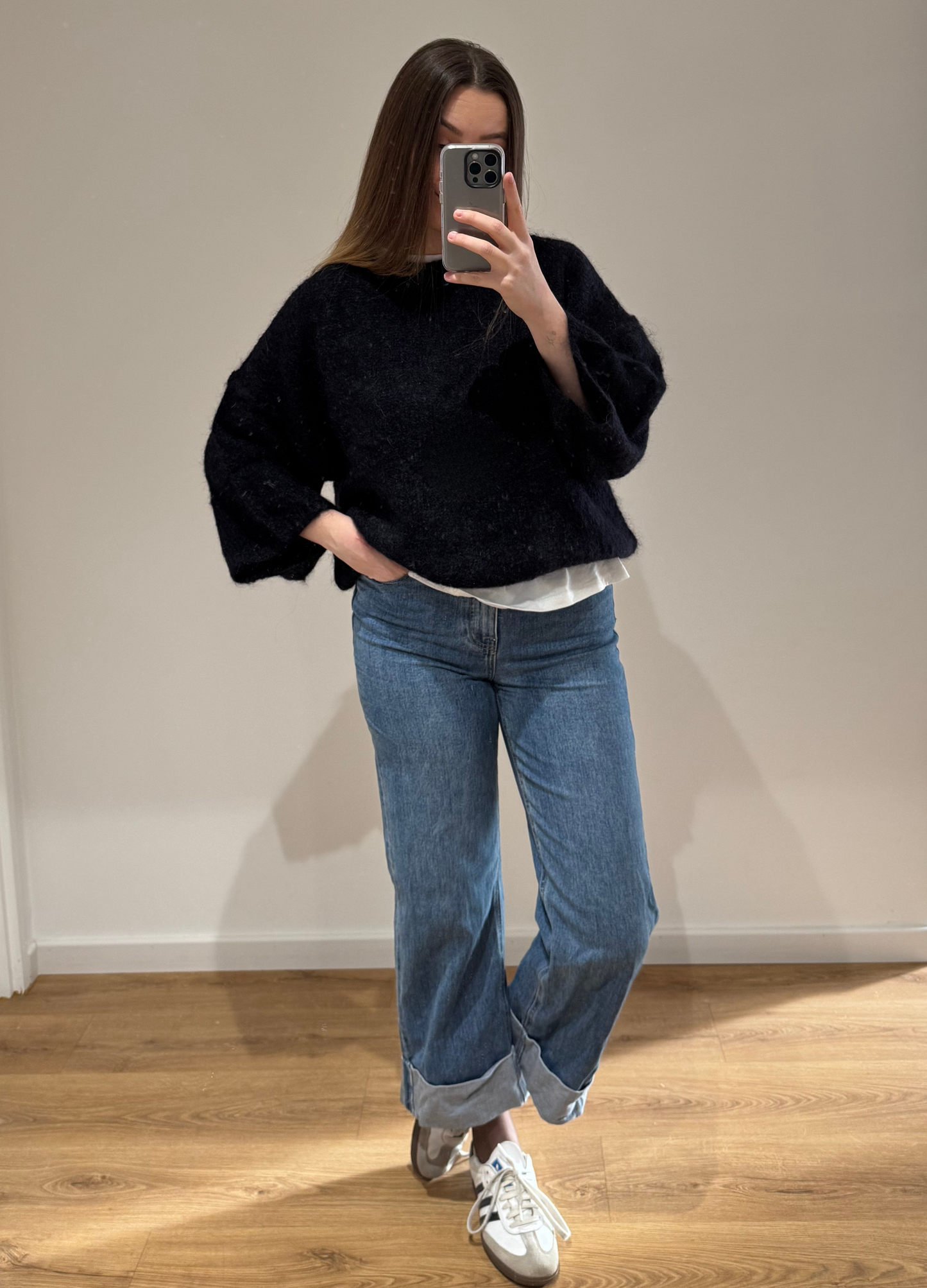 Femme portant un pull noir droit MARYLOU en mohair, avec un jean droit ALEXIA à ourlet , vue en intérieur sur parquet et fond blanc.