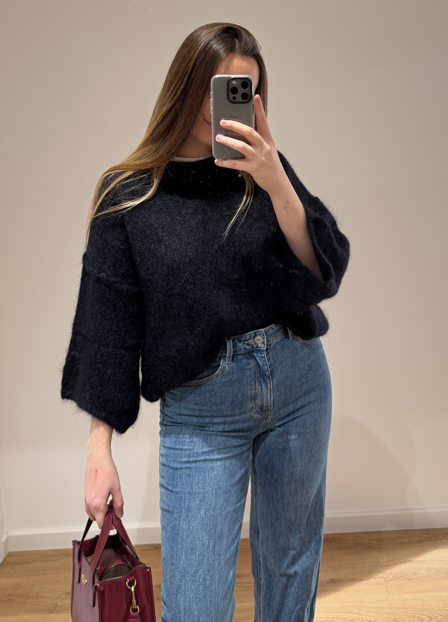 Femme portant un pull noir droit MARYLOU en mohair, avec un jean droit ALEXIA à ourlet , vue en intérieur sur parquet et fond blanc.