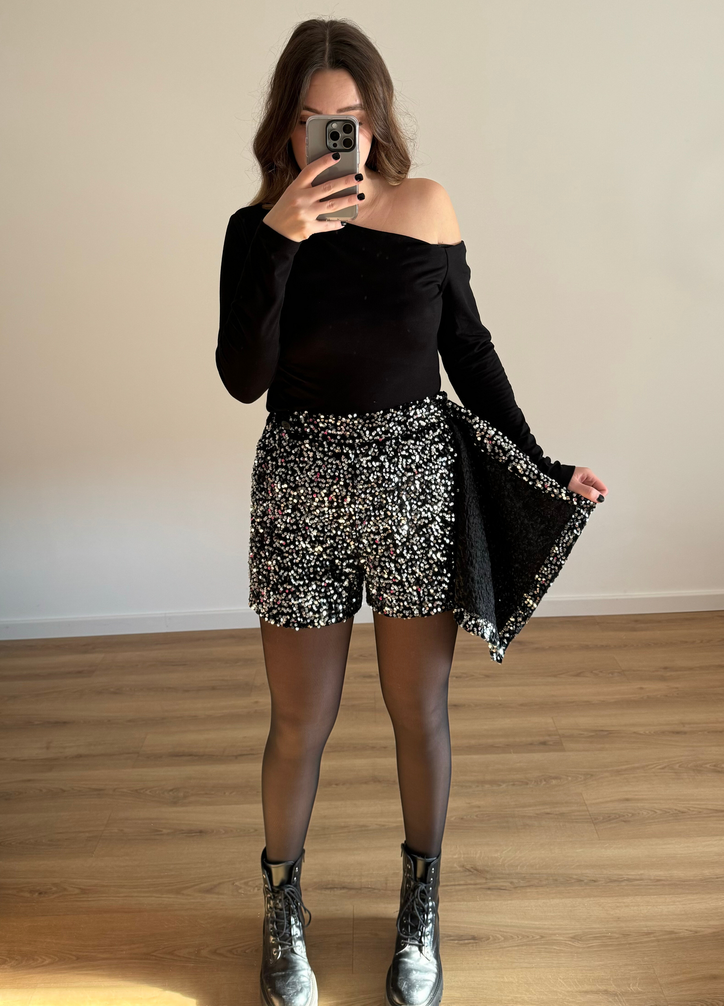Femme posant en selfie, portant un short noir orné de strass étincelants, assorti à un haut élégant. Look glamour et moderne, parfait pour une soirée ou un événement spécial.