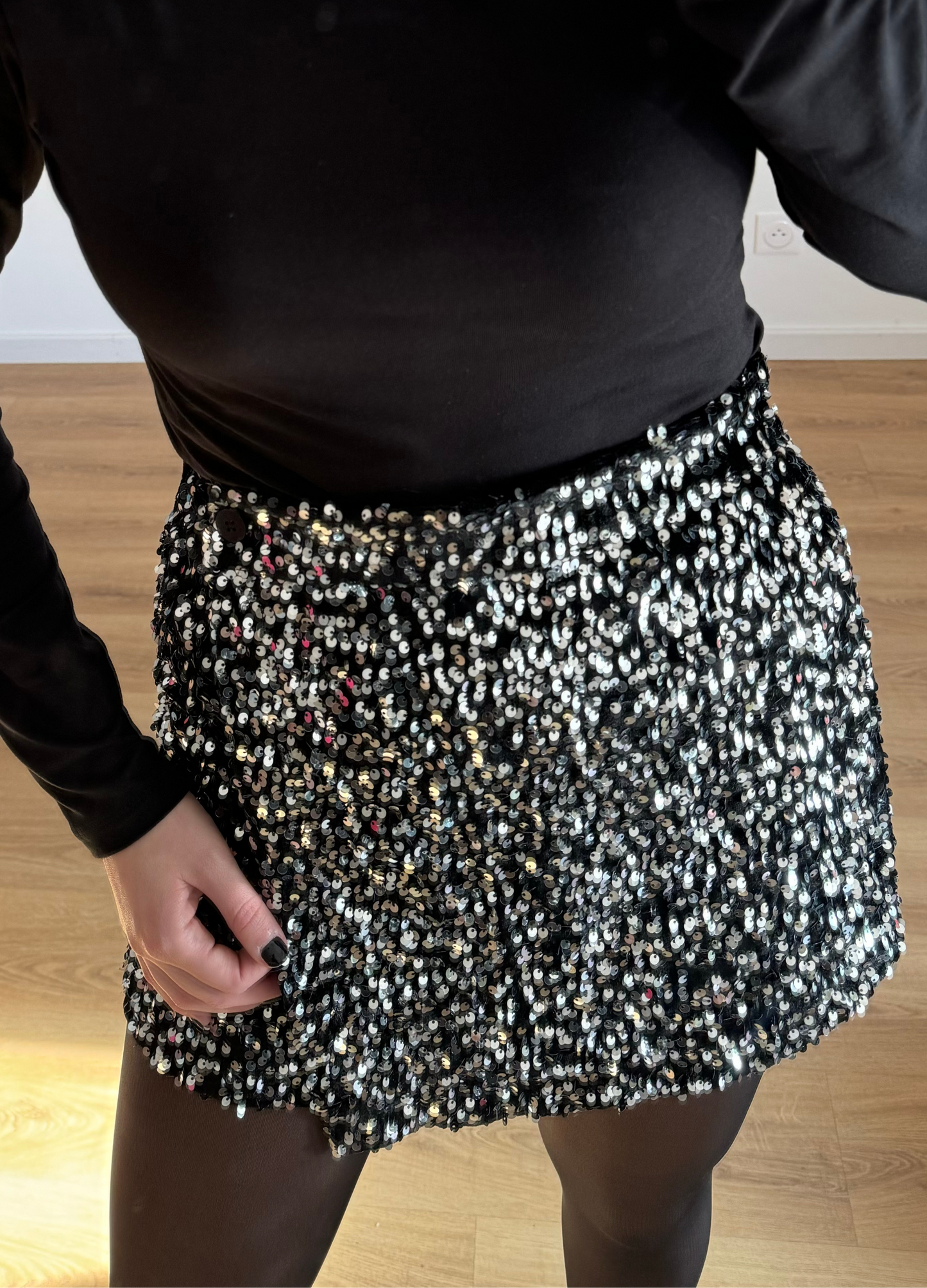 Femme posant en selfie, portant un short noir orné de strass étincelants, assorti à un haut élégant. Look glamour et moderne, parfait pour une soirée ou un événement spécial.