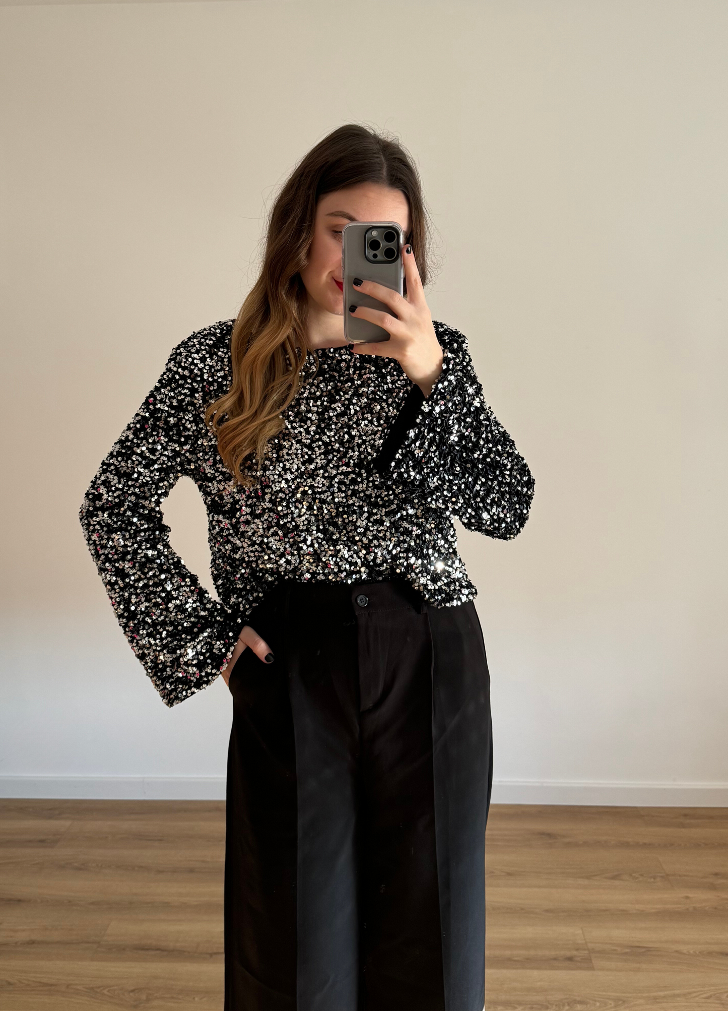 Femme prenant un selfie tout en portant un haut en velour noir à stras à manches longues, associé à un pantalon noir taille haute et ample. Look élégant et intemporel, idéal pour une tenue habillée ou casual chic.