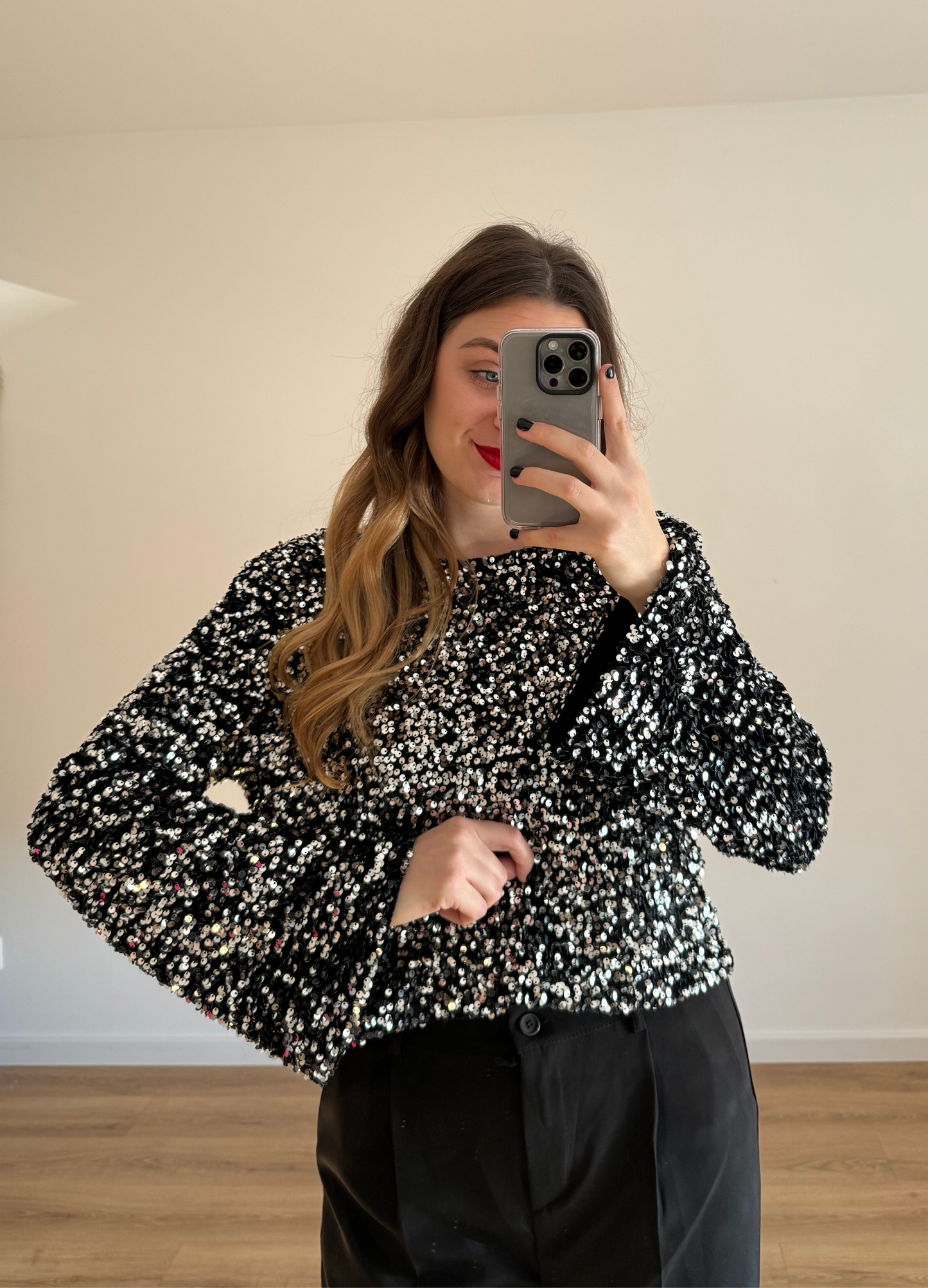 Femme prenant un selfie tout en portant un haut en velour noir à stras à manches longues, associé à un pantalon noir taille haute et ample. Look élégant et intemporel, idéal pour une tenue habillée ou casual chic.