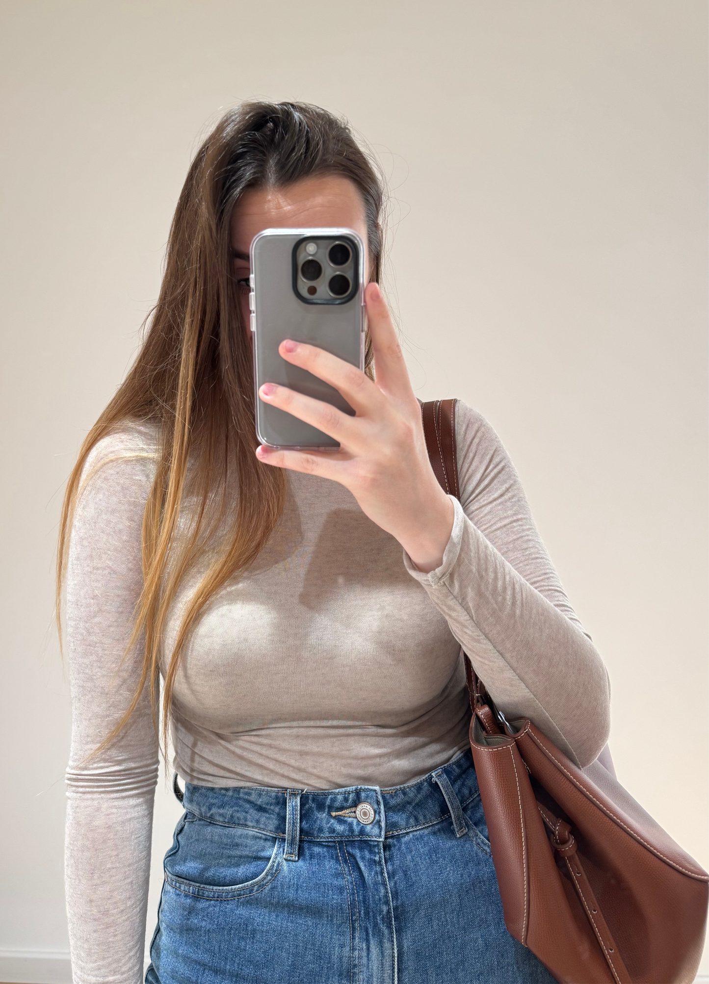 Femme portant un top en cachemire taupe en transparence CAROLINA, avec un jean droit ALEXIA à ourlet, et un sac camer, vue en intérieur avec un fond blanc.