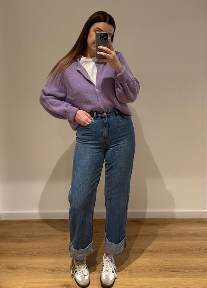 Femme portant un cardigan blanc OLIVIA en coton à boutons argenté, avec un t-shirt blanc CECILE en dessous et un jean droit ALEXIA à ourlet , vue en intérieur sur parquet et fond blanc.