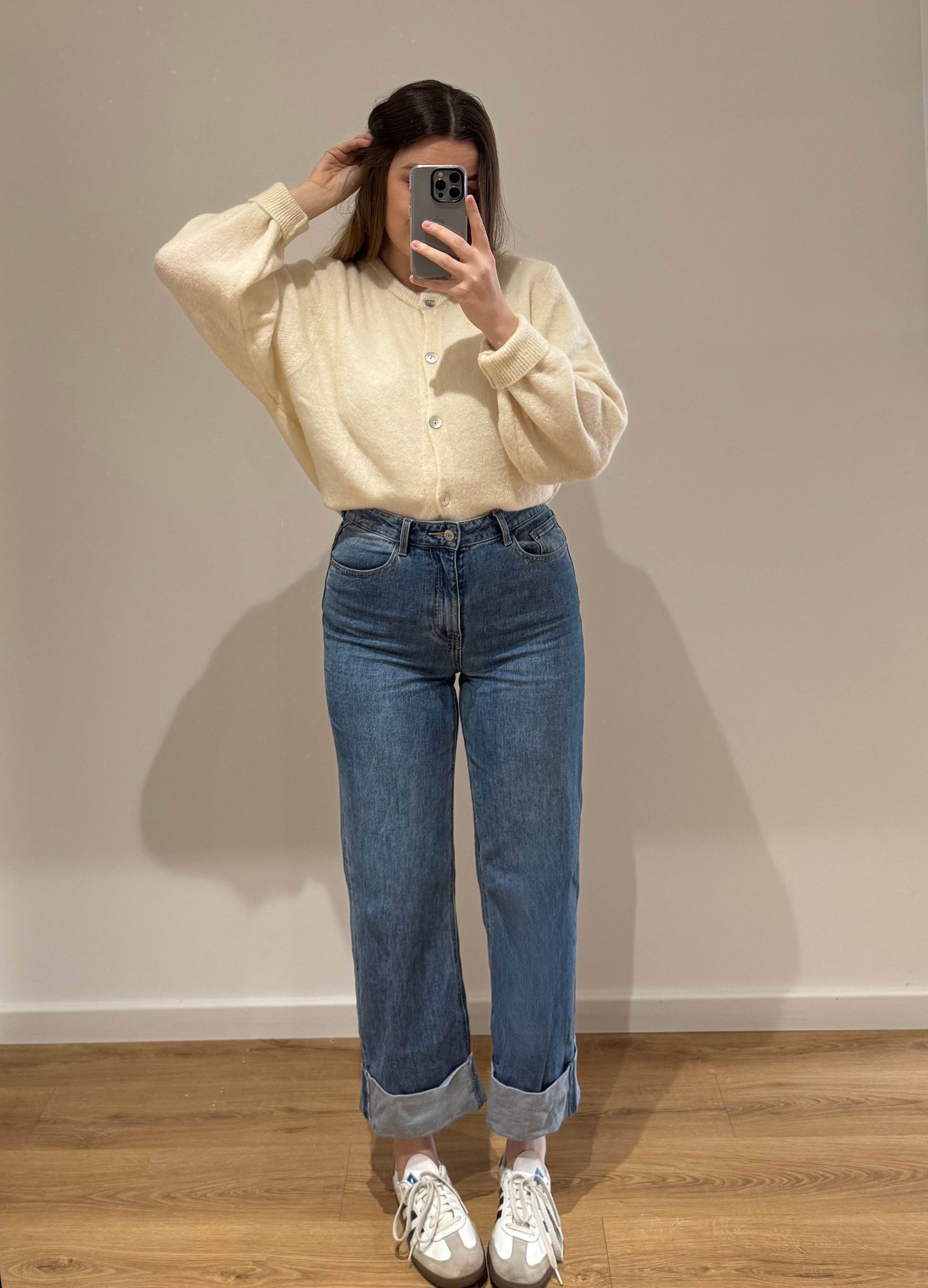 Femme portant un cardigan blanc OLIVIA en coton à boutons argenté, avec un jean droit ALEXIA à ourlet , vue en intérieur sur parquet et fond blanc.