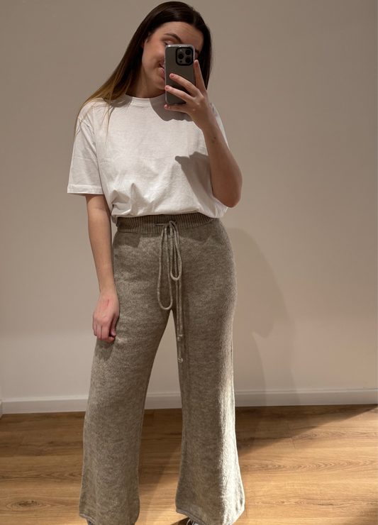 Femme portant un t-shirt blanc CECILE avec un pantalon large beige LEANA en maille, vue en intérieur sur parquet.