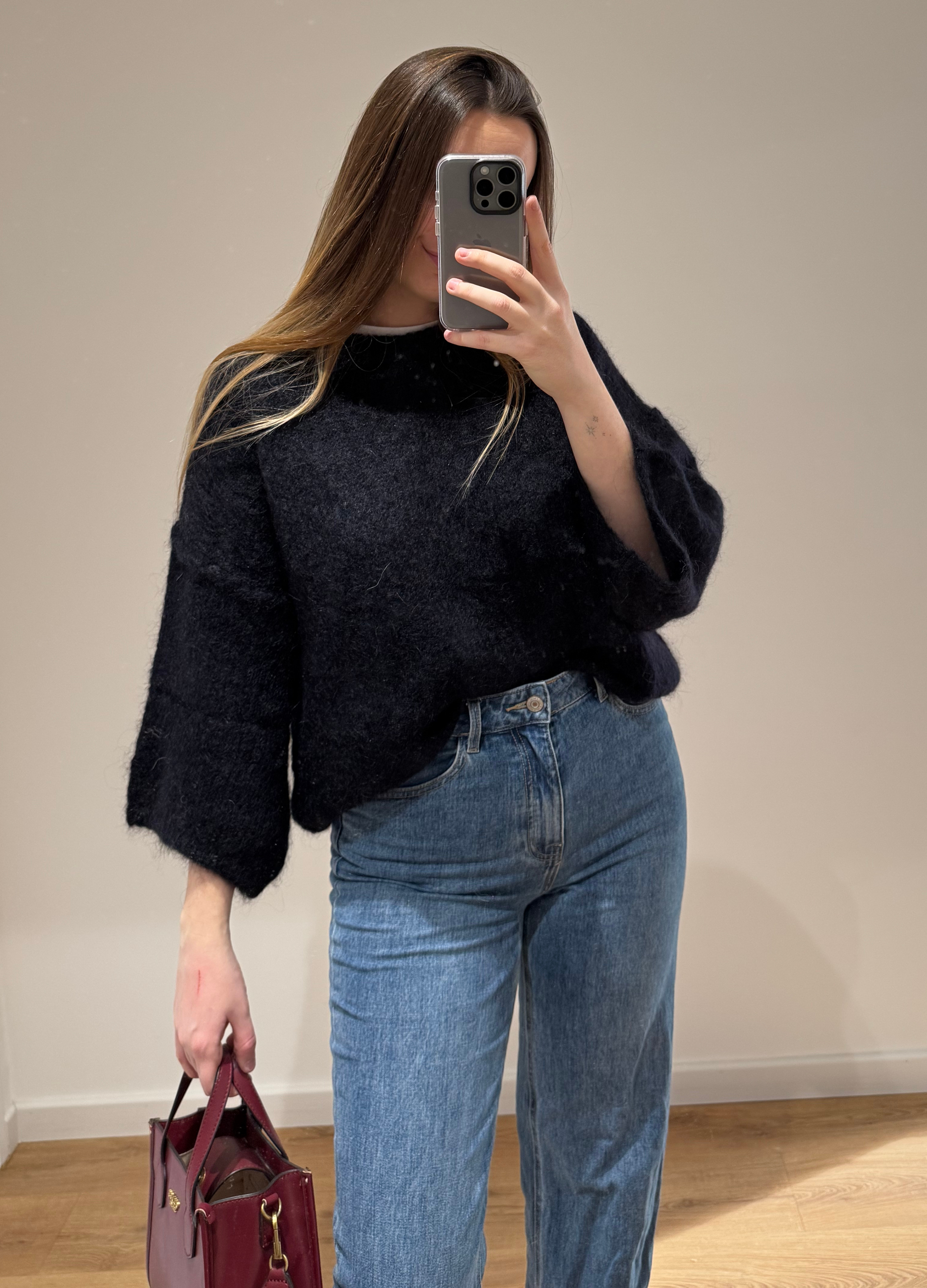 Femme portant un pull noir droit MARYLOU en mohair, avec un jean droit ALEXIA à ourlet , vue en intérieur sur parquet et fond blanc.