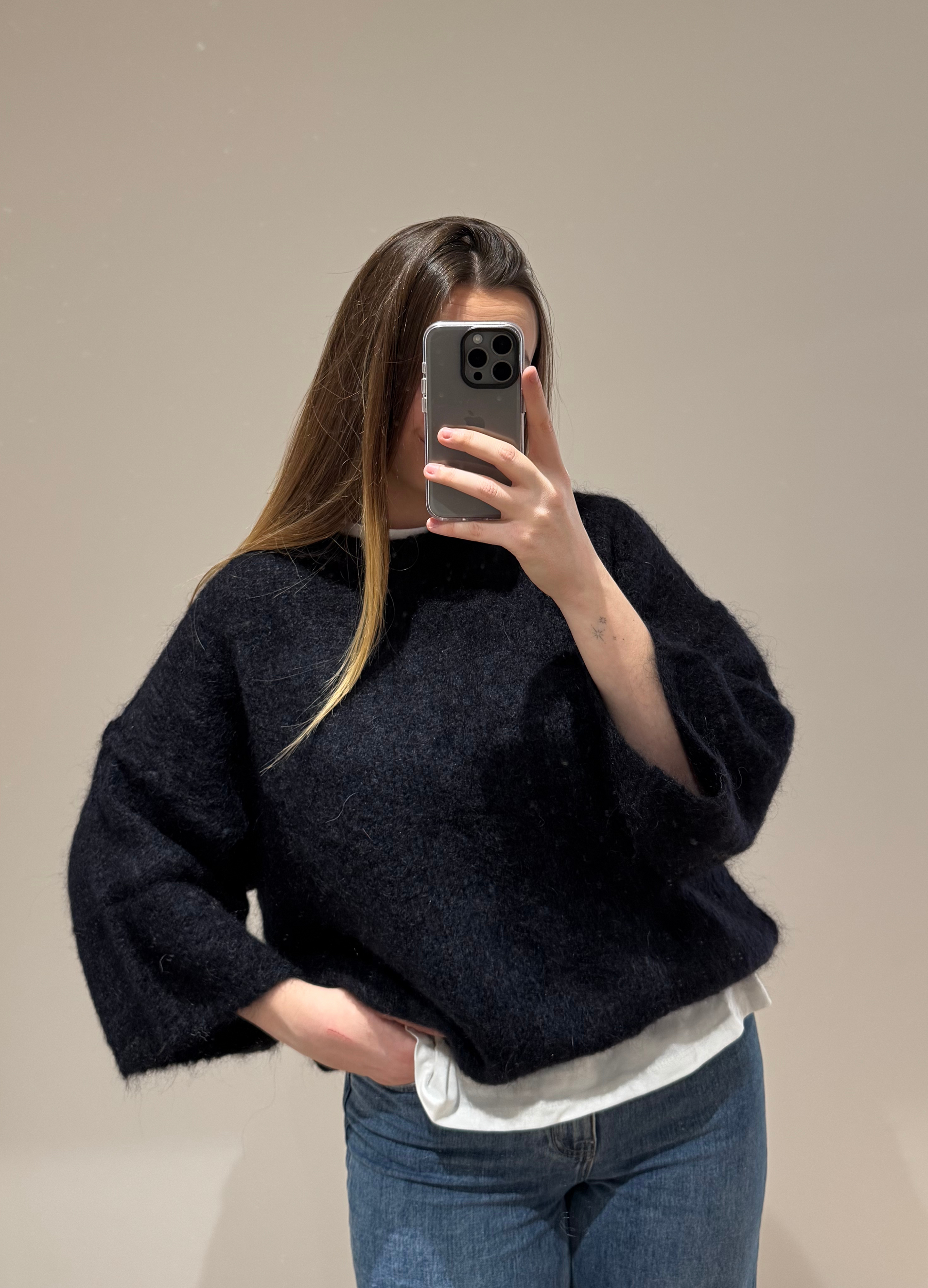 Zoom sur une femme portant un pull noir droit MARYLOU en mohair, avec un jean droit ALEXIA à ourlet , vue en intérieur sur parquet et fond blanc.