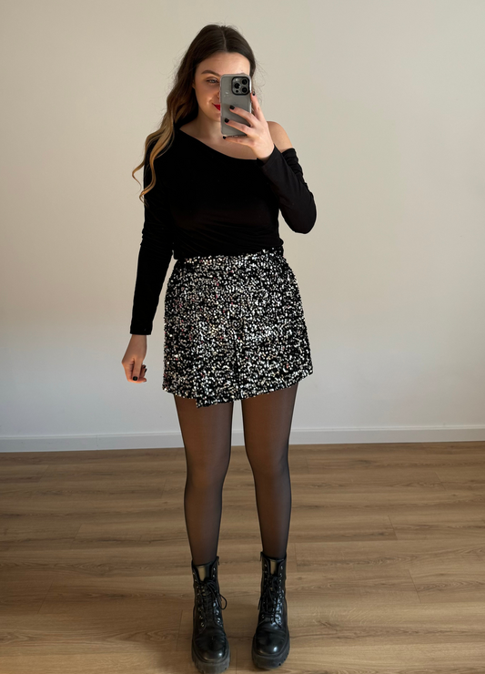 Femme posant en selfie, portant un short noir orné de strass étincelants, assorti à un haut élégant. Look glamour et moderne, parfait pour une soirée ou un événement spécial. 