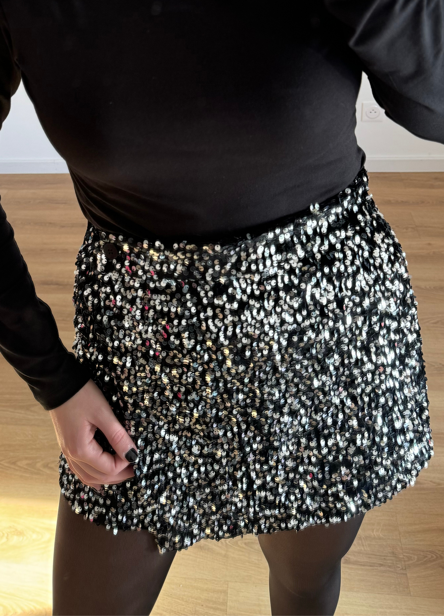 Femme posant en selfie, portant un short noir orné de strass étincelants, assorti à un haut élégant. Look glamour et moderne, parfait pour une soirée ou un événement spécial. 