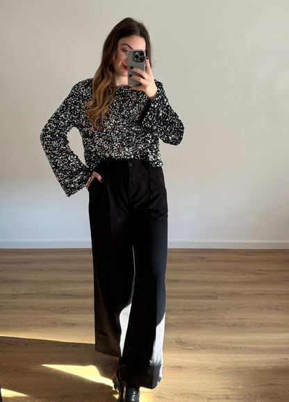 Femme prenant un selfie tout en portant un haut en velour noir à stras à manches longues, associé à un pantalon noir taille haute et ample. Look élégant et intemporel, idéal pour une tenue habillée ou casual chic. 