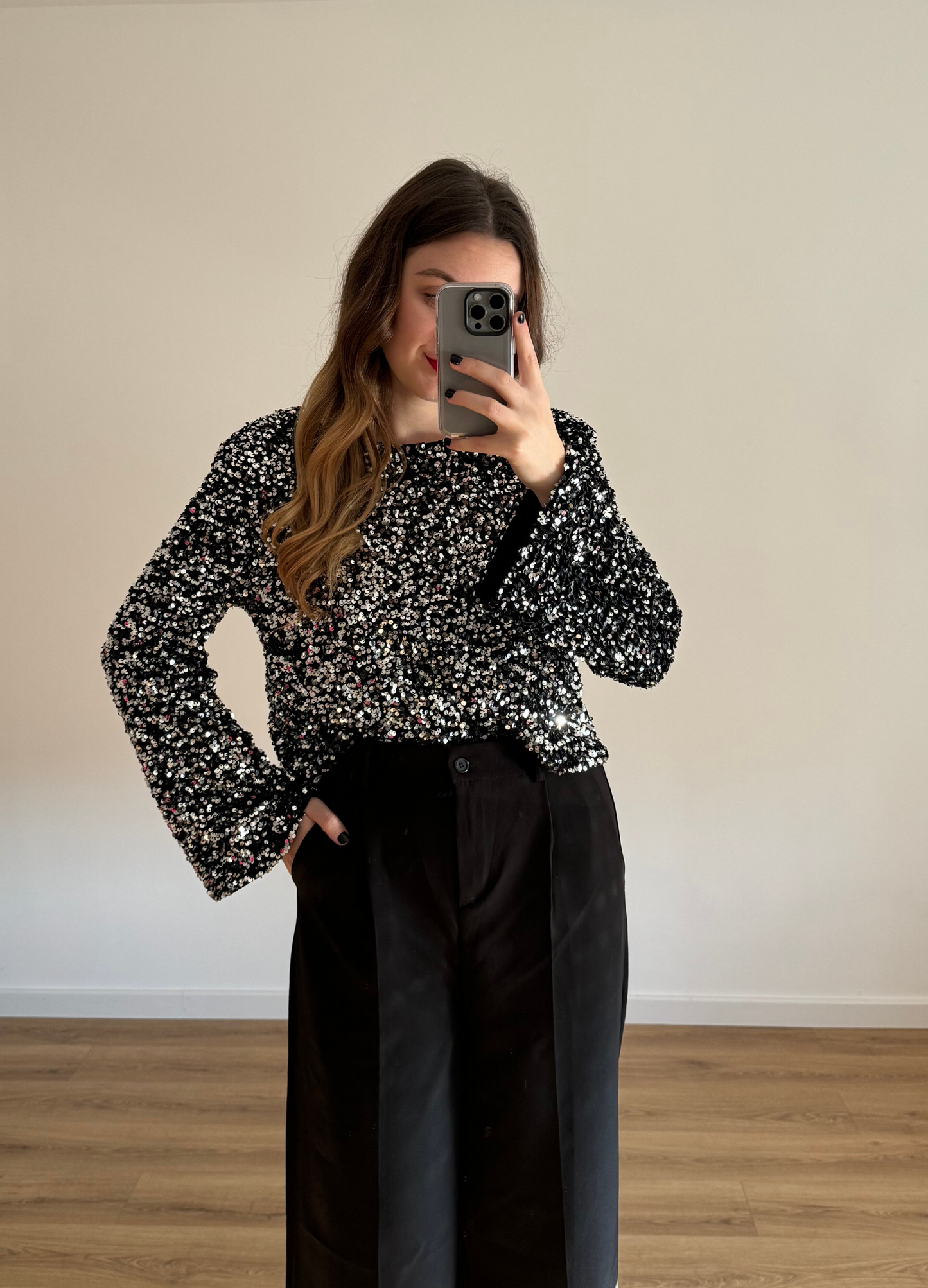 Femme prenant un selfie tout en portant un haut en velour noir à stras à manches longues, associé à un pantalon noir taille haute et ample. Look élégant et intemporel, idéal pour une tenue habillée ou casual chic. 