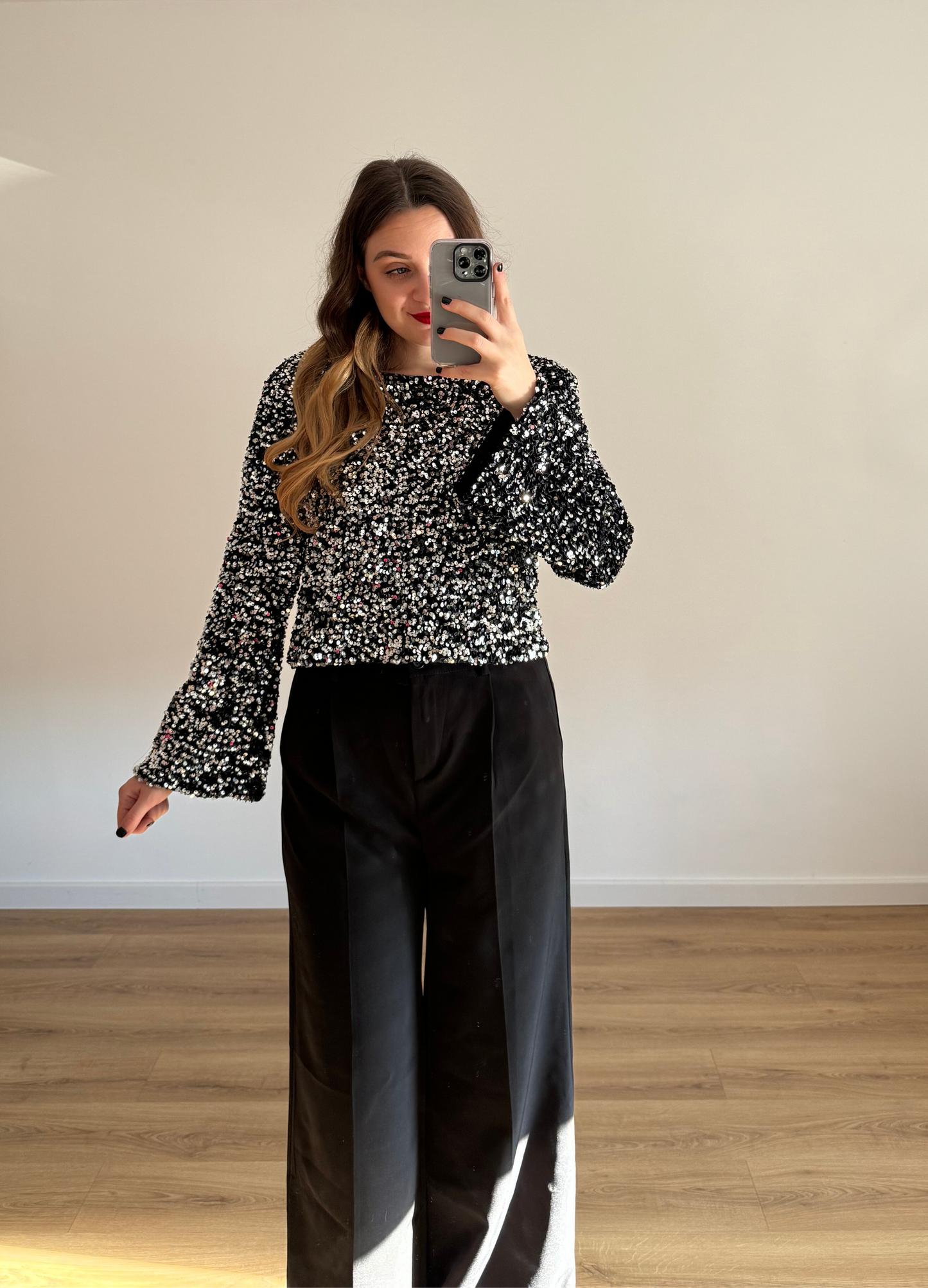 Femme prenant un selfie tout en portant un haut en velour noir à stras à manches longues, associé à un pantalon noir taille haute et ample. Look élégant et intemporel, idéal pour une tenue habillée ou casual chic. 