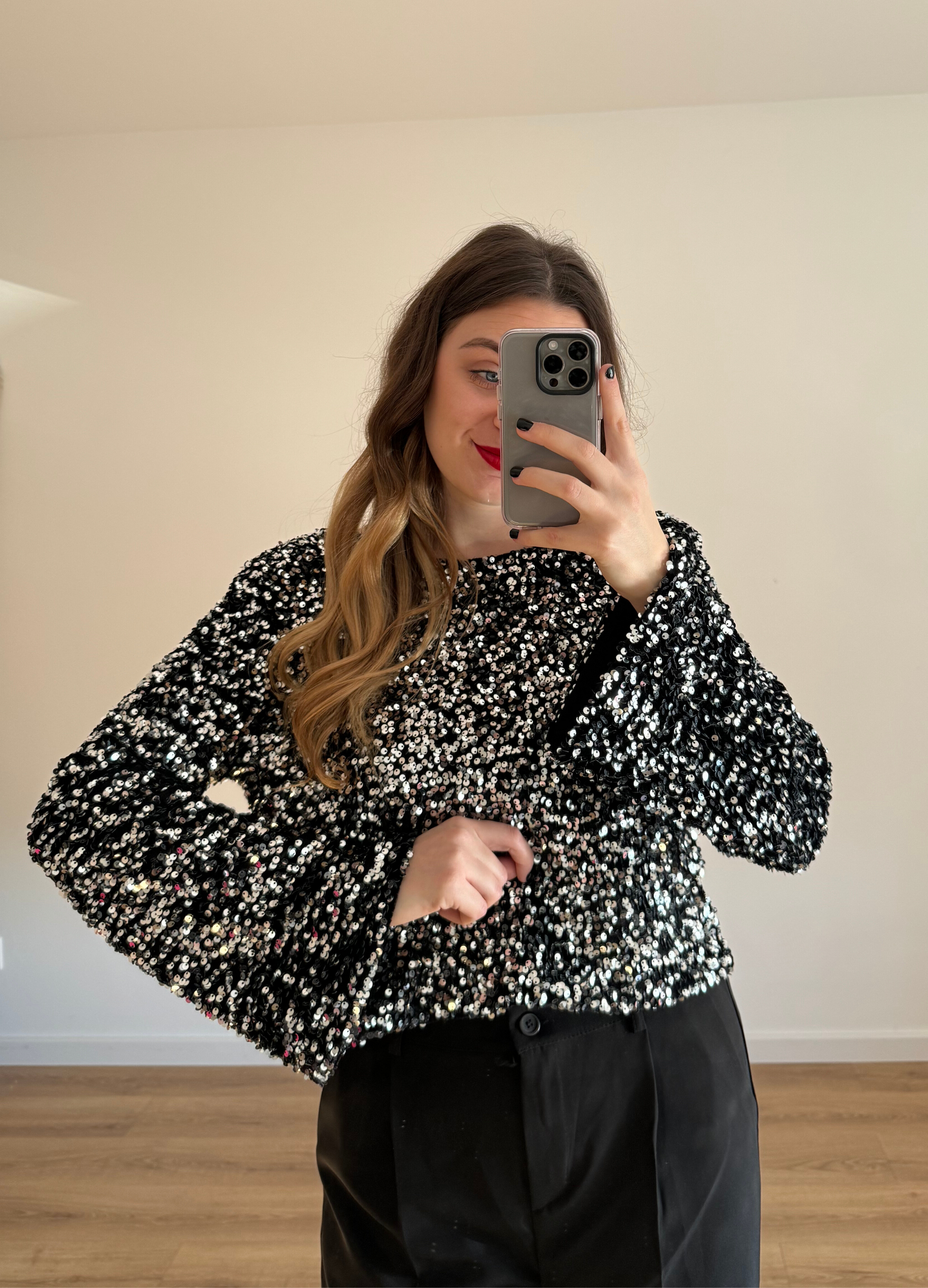 Femme prenant un selfie tout en portant un haut en velour noir à stras à manches longues, associé à un pantalon noir taille haute et ample. Look élégant et intemporel, idéal pour une tenue habillée ou casual chic. 