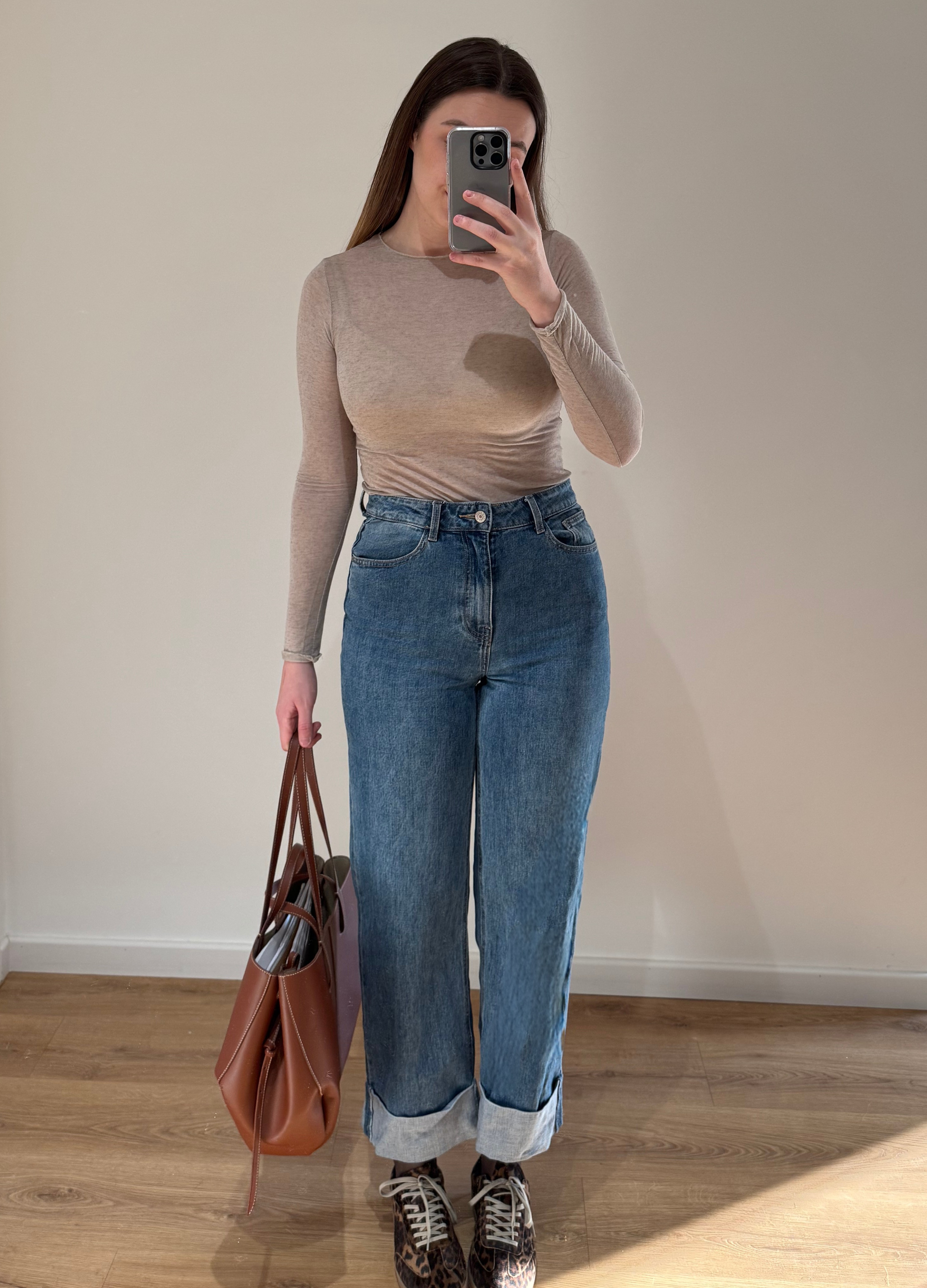 Femme portant un top en cachemire taupe en transparence CAROLINA, avec un jean droit ALEXIA à ourlet, et un sac camel, vue en intérieur sur parquet et fond blanc.