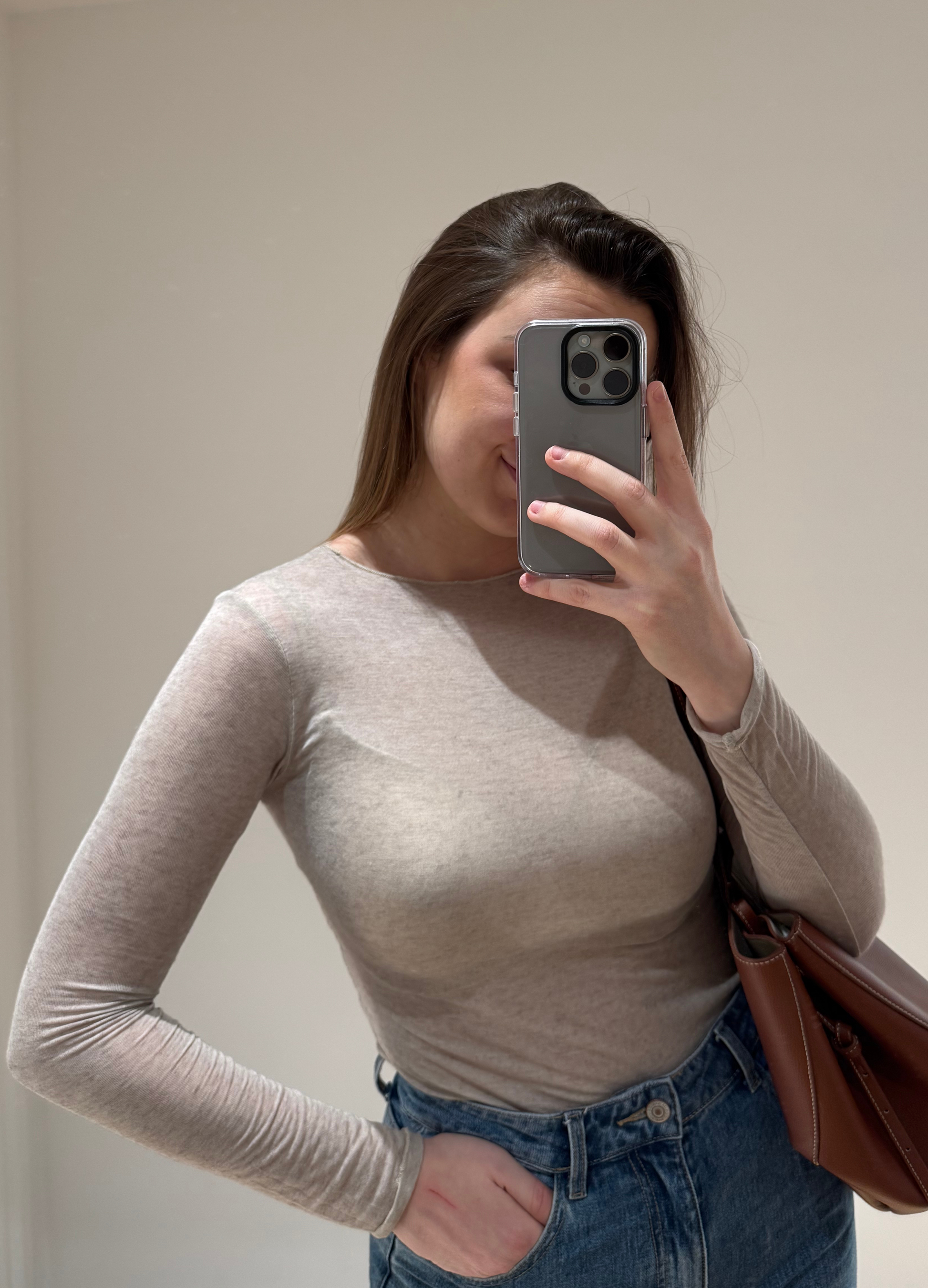 Femme portant un top en cachemire taupe en transparence CAROLINA, avec un jean droit ALEXIA à ourlet, et un sac camel, vue en intérieur sur parquet et fond blanc.