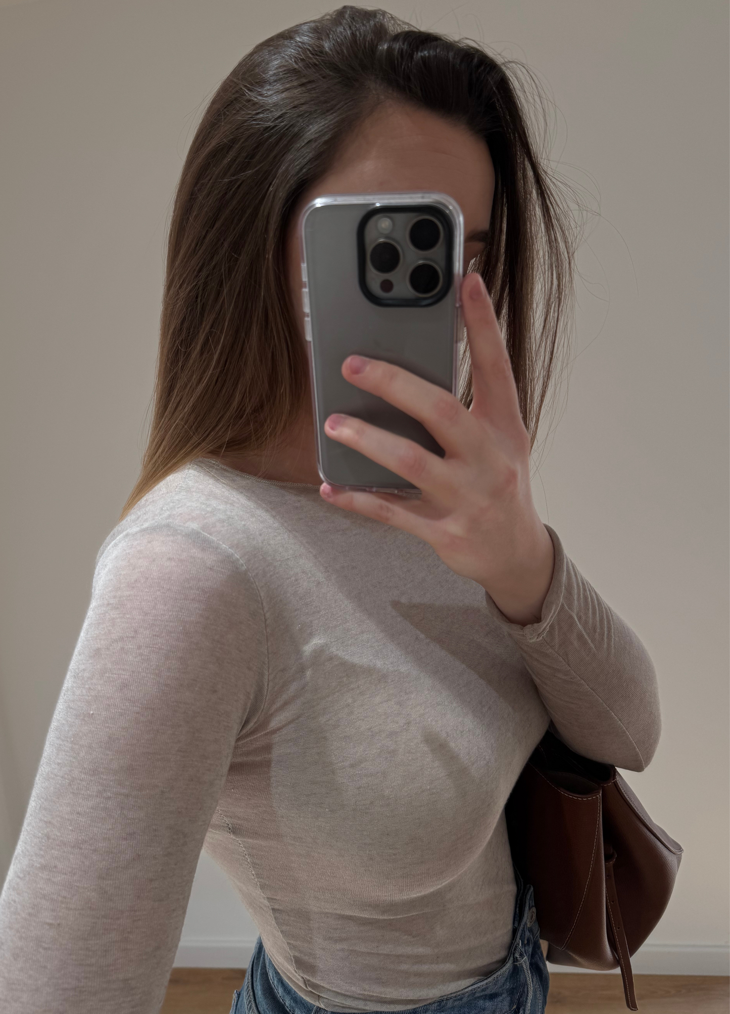 Zoom sur une femme portant un top en cachemire taupe en transparence CAROLINA, avec un jean droit ALEXIA à ourlet, et un sac camel, vue en intérieur sur parquet et fond blanc.